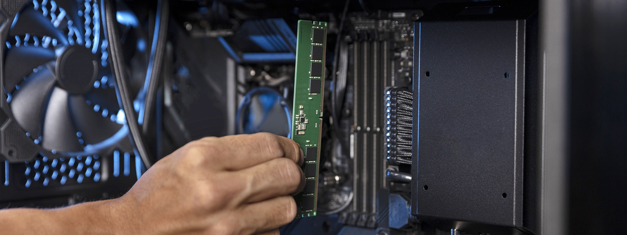 A person's hand is holding a green RAM memory card in front of a computer's motherboard.