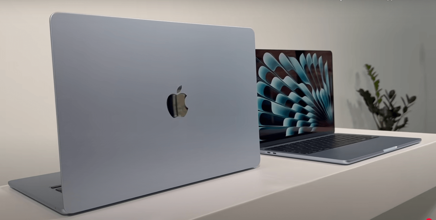 two Apple MacBook laptops placed on a white surface, with one laptop displaying a colorful fan-like wallpaper and the other laptop showing a plain white background.