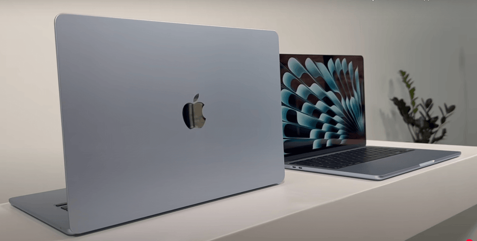 two Apple MacBook laptops placed on a white surface, with one laptop displaying a colorful fan-like wallpaper and the other laptop showing a plain white background.