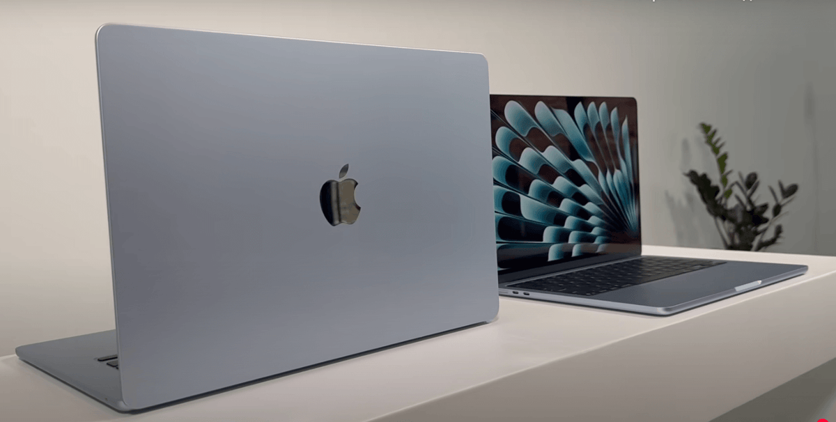 two Apple MacBook laptops placed on a white surface, with one laptop displaying a colorful fan-like wallpaper and the other laptop showing a plain white background.